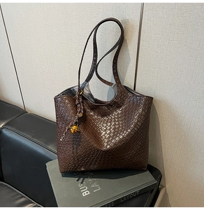 Détail d'un sac cabas marron foncé en cuir tressé avec élégant pendentif cloche doré