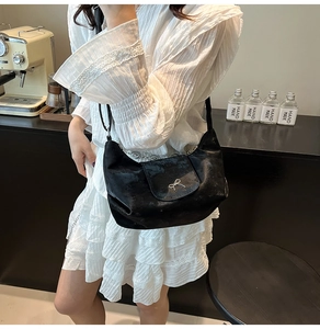 Détail d'un sac demi-lune en velours noir avec nœud en métal argenté sur robe blanche