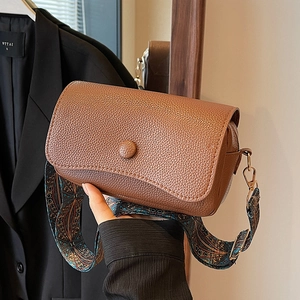 Brown lychee leather crossbody bag with vintage ethnic print wide strap shown held by hand