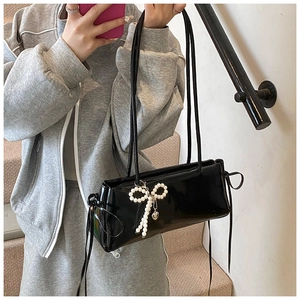 Detail of black glossy shoulder bag with pearl bow charm and heart metal pendant decor