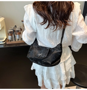 Détail d'un sac bandoulière en similicuir noir avec une boucle nœud papillon argentée