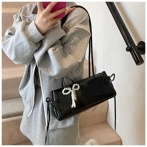 Detail of glossy black patent leather shoulder bag featuring a pearl bow pendant