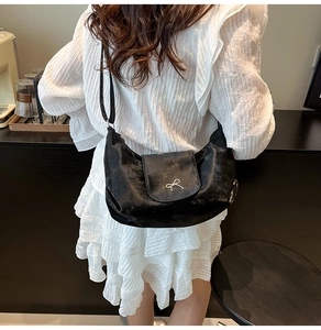 Détail d'un sac bandoulière noir en forme de croissant avec boucle nœud argentée