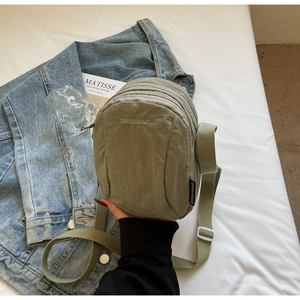 Détail d'un sac bandoulière en nylon vert sauge avec trois compartiments zippés