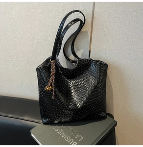 Détail du sac cabas noir à texture crocodile avec corde tressée et pendentif clochette dorée