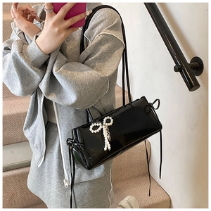 Detail of black patent leather baguette bag featuring a pearl bow charm and side ribbon