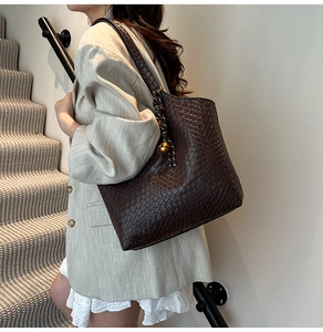 Détail du sac cabas tressé marron foncé avec pendentif sphère dorée sur la bandoulière