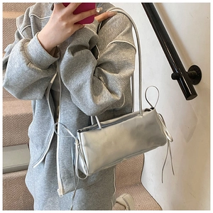 Silver metallic shoulder bag with long straps and tassel detail worn by model on stairs
