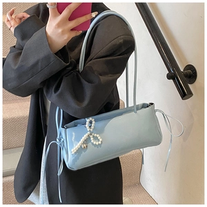 Detail of light blue glossy shoulder bag featuring pearl bow and silver heart pendant