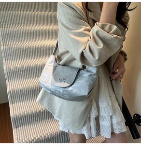 Détail du sac à bandoulière argenté métallisé avec nœud doré porté par un modèle