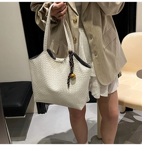 Détail du sac cabas blanc tissé avec motif texturé et pendentif de cloche dorée