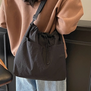 Large black drawstring bucket bag worn cross-body by a model in casual street style