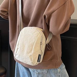 Petit sac bandoulière minimaliste en nylon beige avec sangle réglable porté par un mannequin
