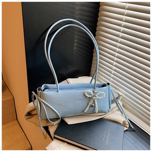 Detail of light blue glossy underarm bag with decorative pearl bow and heart charm
