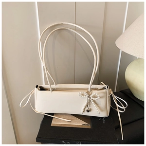 Detail of cream baguette bag featuring pearl bow charm and side drawstring accents