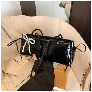 Detail of glossy black underarm bag featuring a pearl bow charm and sleek patent leather