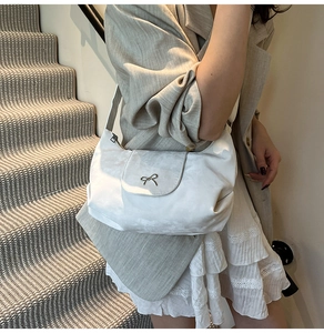 Détail d'un sac à bandoulière blanc avec nœud argenté et sangle ajustable sur un modèle