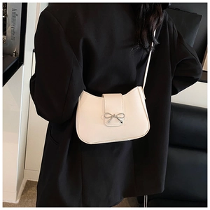 Off-white crossbody bag with silver bow accent worn over a black blazer for a chic look
