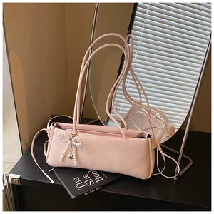 Detail of a pink underarm bag featuring a pearl bow charm and smooth leather texture