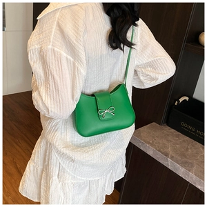 Detail of green crescent shoulder bag with silver bow ornament on white dress
