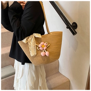 Close-up of khaki woven bucket bag with white lace bow and pink flower cherry pendant