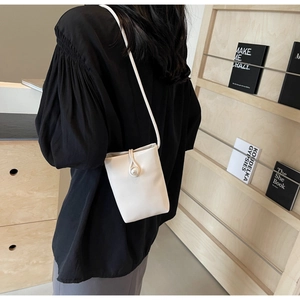 Close-up of white mini crossbody phone bag with pearl button on minimalist wood background
