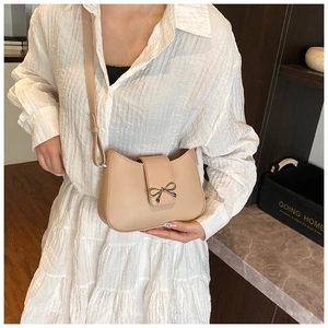Close-up of beige leather baguette bag with a silver metal bow buckle detail