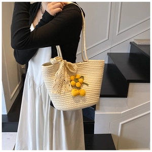 Close-up of cream woven shoulder bag featuring lace bow and yellow knit floral charms