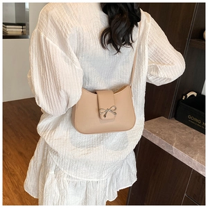 Close-up of minimalist beige baguette bag with silver bow buckle on white dress