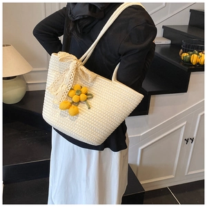 Detailed close-up of a white straw bag with lace bow and yellow flower charm on model