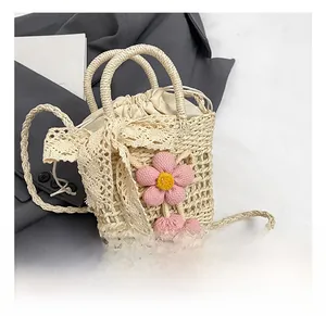 Detail of beige straw bag featuring lace bow, knit flower charm and crossbody strap