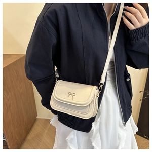 Detail of cream crossbody bag with metal bow buckle worn by model in casual style
