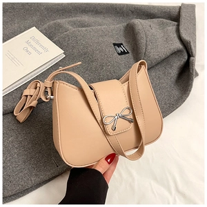 Detail of beige shoulder bag featuring silver bow buckle and adjustable strap