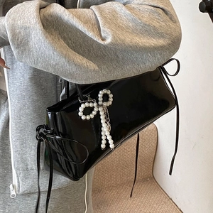 Glossy black patent leather underarm bag with pearl accents and decorative ribbon bows