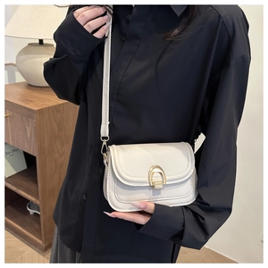 Detail of a creamy white crossbody bag with a distinctive golden horseshoe lock closure