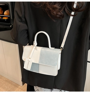 Detailed view of bicolor crossbody bag with fashion tag held by a model in kitchen setting