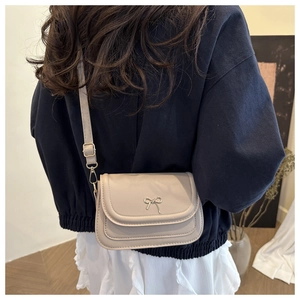Detail of elegant beige crossbody bag with metallic bow clasp shown on a model