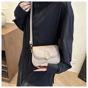Detailed view of beige crossbody square bag featuring a gold arch buckle on a model