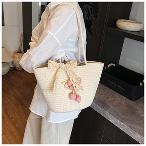 Detail of cream woven bucket bag featuring lace bow and pink knitted cherry charm