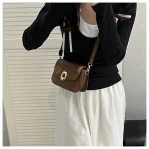 Close-up of a vintage dark brown leather crossbody bag with a golden horseshoe buckle