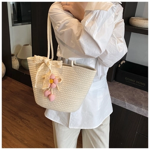 Detail of hand-woven cream tote bag with crochet flower pendant and lace bow