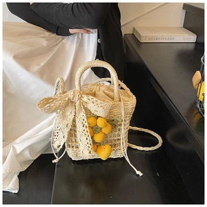 Detail of beige hand-woven straw bucket bag with lace bow and yellow floral charms