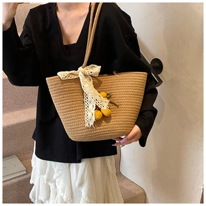 Detail of straw woven tote bag with white lace bow and crochet orange fruit charm