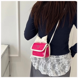 Detail of fuchsia crocodile pattern crossbody bag with a large cream white bow accent