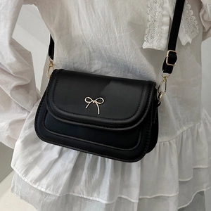 Chic black crossbody bag with gold bow ornament and elegant wave stitching on white shirt