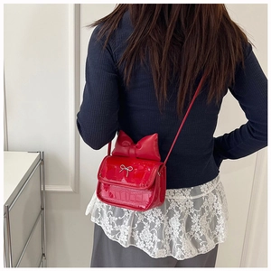 Detail of red croc-effect patent leather shoulder bag with decorative bow and metal clasp