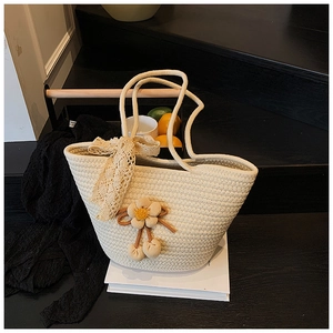 Detailed view of woven beige bucket bag with lace bow and floral pendant on books