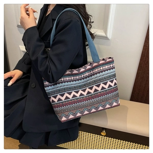 Detail of ethnic canvas tote bag with geometric patterns and blue woven handles on a model