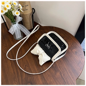 Detail of a contrast color mini crossbody bag with a large white bow on a wooden table