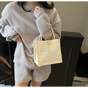 Dettaglio borsa pranzo in tela beige con bottone in legno e trama trapuntata su modella